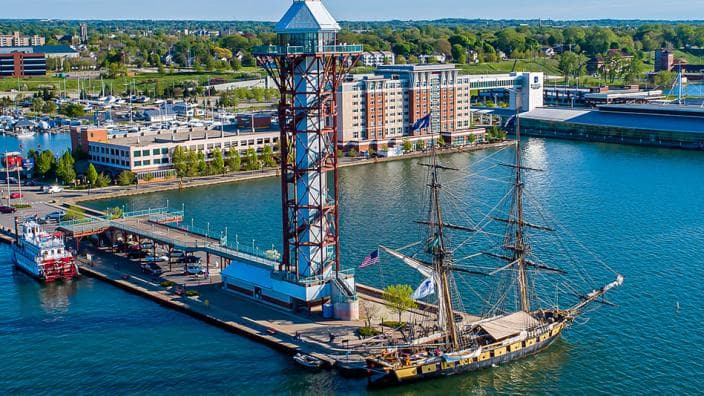 Tall lattice observation tower and a historic sailing ship docked at a sunny waterfront.
