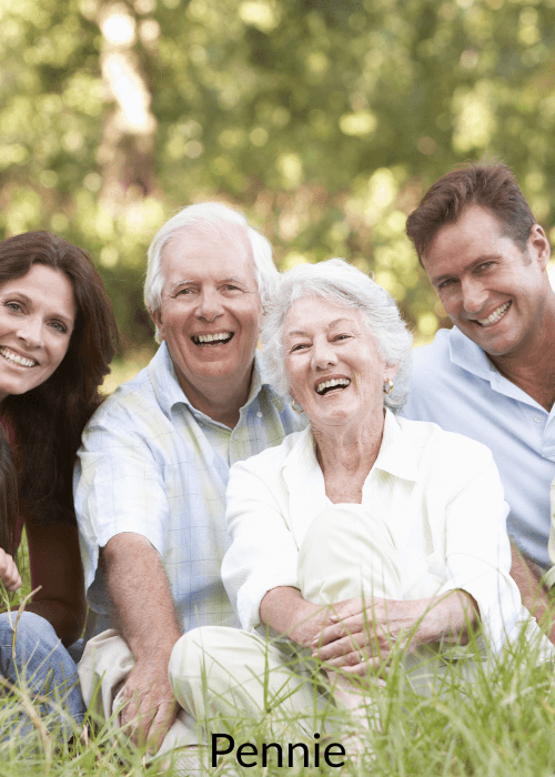 A joyful multi-generational family sits in the grass, smiling and laughing together outdoors.